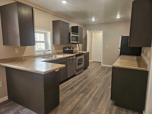 kitchen with kitchen peninsula, dark wood-type flooring, appliances with stainless steel finishes, and sink