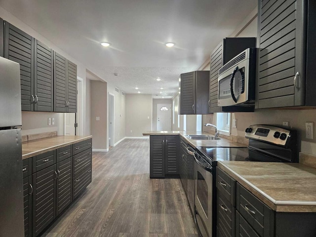 kitchen with stainless steel appliances, kitchen peninsula, a textured ceiling, dark hardwood / wood-style flooring, and sink