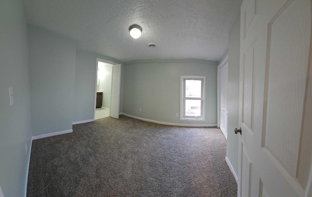 unfurnished room with a textured ceiling and dark colored carpet