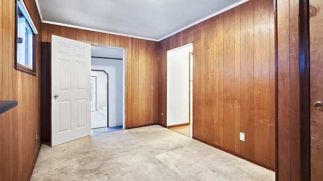 empty room featuring wooden walls, light carpet, and crown molding