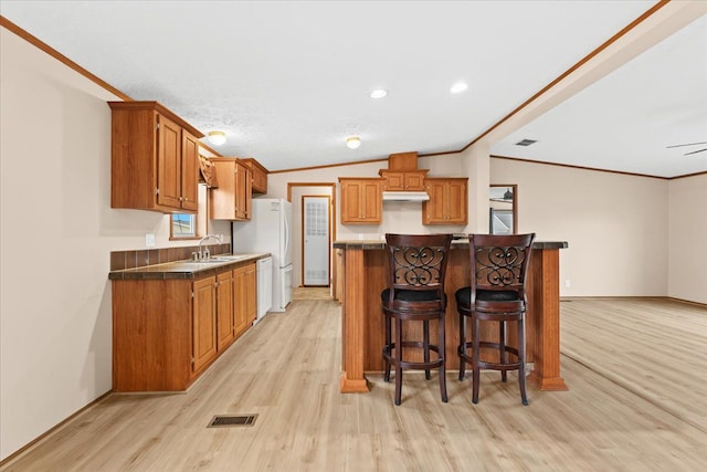 kitchen featuring white appliances, a kitchen breakfast bar, light hardwood / wood-style floors, crown molding, and lofted ceiling