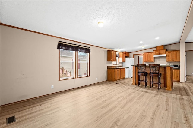 kitchen featuring white refrigerator, lofted ceiling, a kitchen breakfast bar, light hardwood / wood-style flooring, and a kitchen island