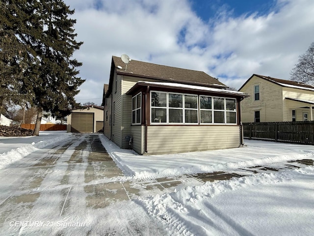 snow covered property with a sunroom, a garage, and an outdoor structure