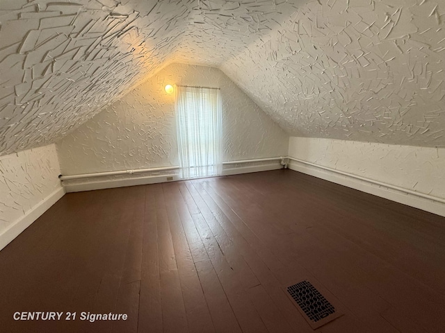 additional living space with a textured ceiling, dark wood-type flooring, and lofted ceiling