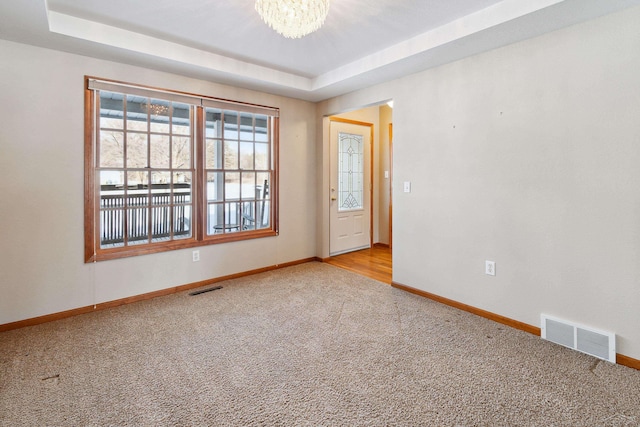 carpeted empty room featuring a tray ceiling and a notable chandelier