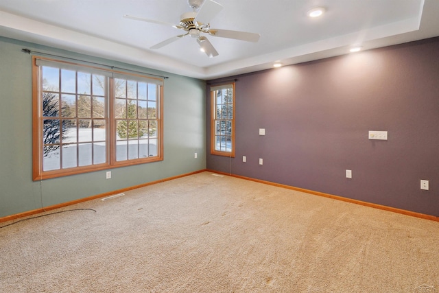 carpeted spare room with a raised ceiling and ceiling fan