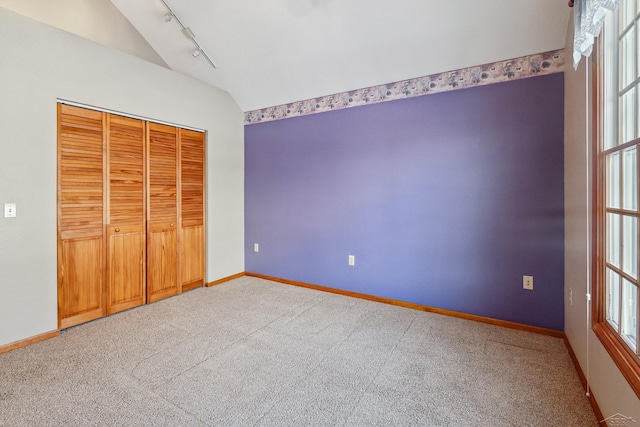 unfurnished bedroom with track lighting, vaulted ceiling, a closet, and carpet flooring