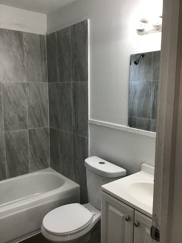 bathroom with tub / shower combination, toilet, vanity, and a textured wall