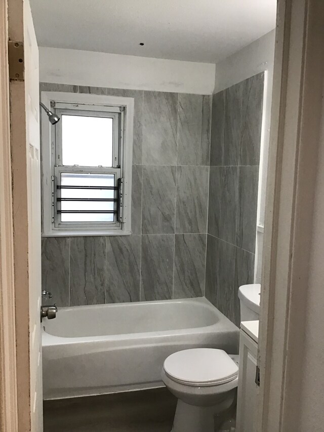 full bathroom featuring vanity, tiled shower / bath, and toilet