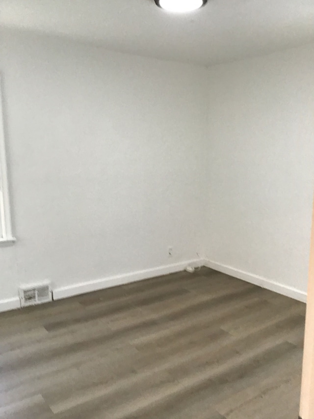 spare room with dark wood-style floors, visible vents, and baseboards