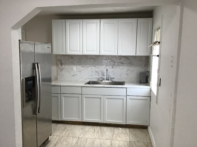 kitchen featuring stainless steel fridge with ice dispenser, light countertops, decorative backsplash, marble finish floor, and a sink