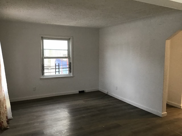 spare room with a textured ceiling, dark wood-style flooring, and baseboards