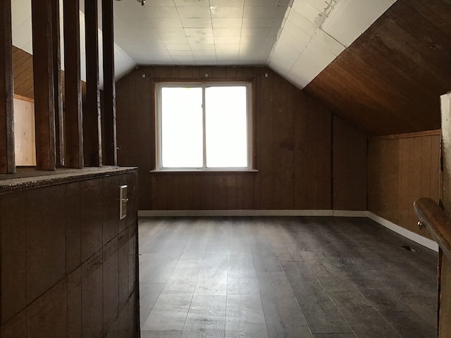 bonus room featuring lofted ceiling, wooden walls, baseboards, and wood finished floors