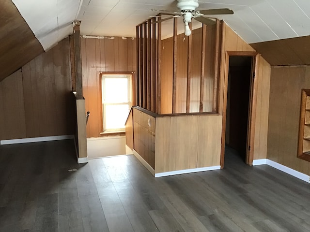 additional living space with wooden walls, baseboards, lofted ceiling, ceiling fan, and dark wood-type flooring