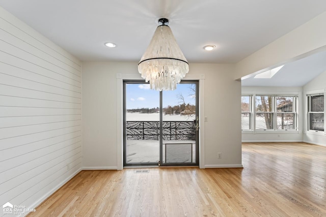 unfurnished dining area with a skylight, wooden walls, light wood-type flooring, and a notable chandelier