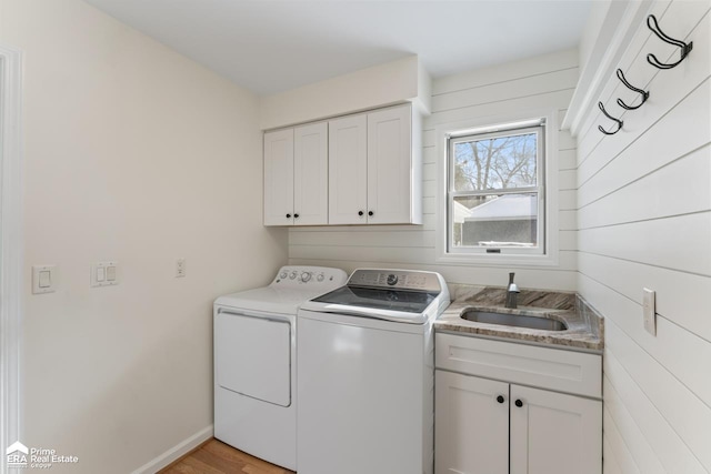 clothes washing area with light hardwood / wood-style flooring, washer and clothes dryer, wood walls, cabinets, and sink