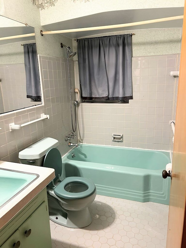 full bathroom with tile walls, tiled shower / bath combo, vanity, tile patterned floors, and toilet