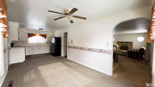 kitchen with sink, black fridge, white cabinetry, and light carpet