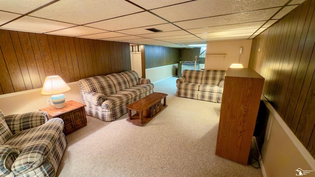 living room featuring a paneled ceiling, wooden walls, and carpet floors