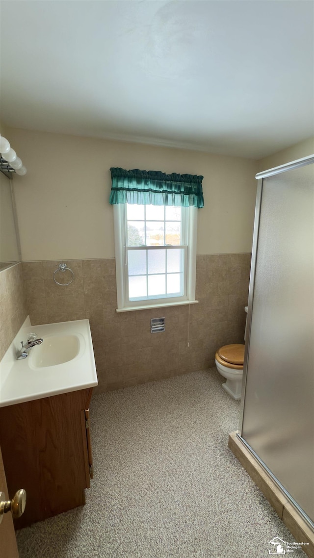 bathroom featuring tile walls, a shower with door, vanity, and toilet