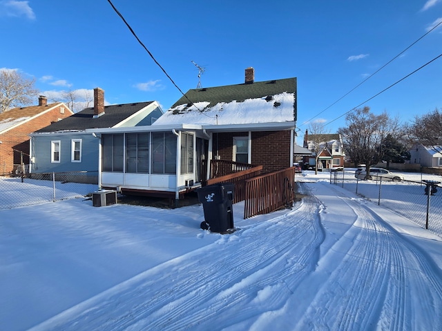 snow covered rear of property with central AC and a sunroom