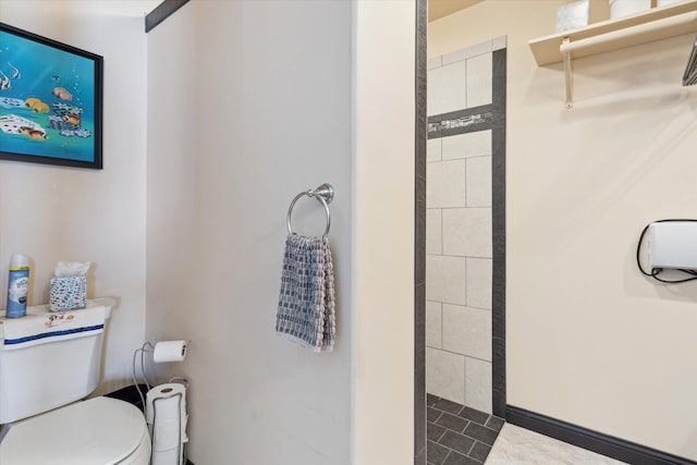 bathroom with toilet, a tile shower, and tile patterned flooring