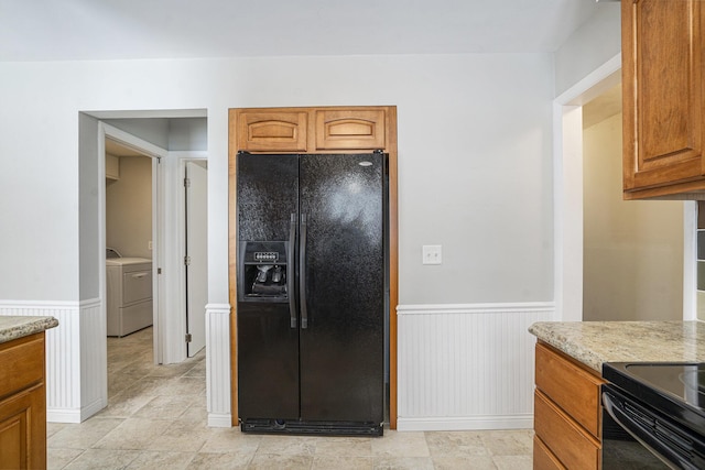 kitchen with black refrigerator with ice dispenser, washer / dryer, and light stone counters