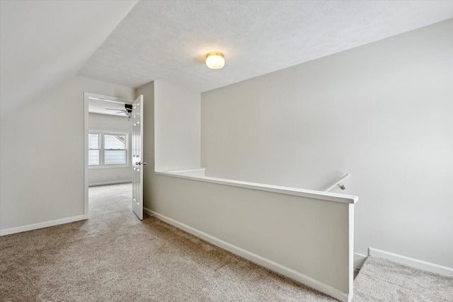 hallway with a textured ceiling, light carpet, and vaulted ceiling