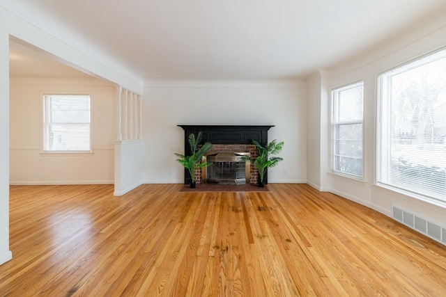 unfurnished living room featuring a brick fireplace, light wood-type flooring, ornamental molding, and a healthy amount of sunlight