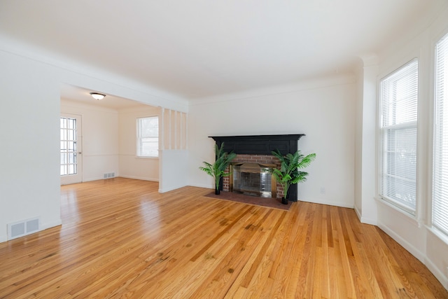 unfurnished living room with a brick fireplace, light wood-type flooring, and ornamental molding