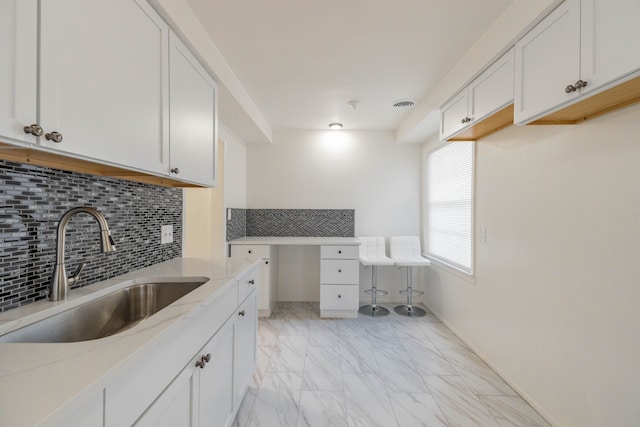 kitchen featuring light stone counters, white cabinets, tasteful backsplash, and sink