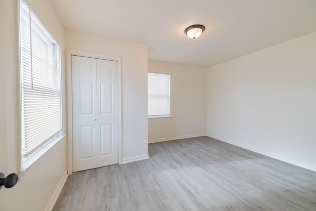 unfurnished bedroom with light hardwood / wood-style flooring, a closet, and multiple windows