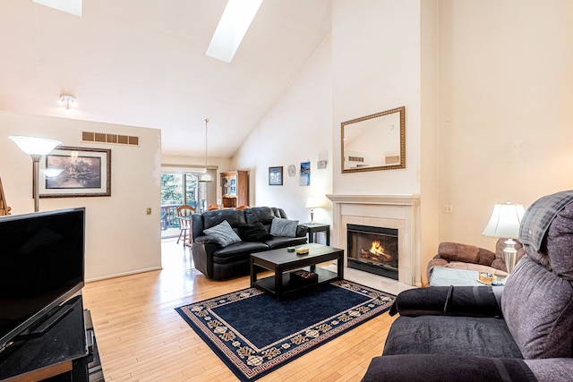 living room with high vaulted ceiling, a skylight, and light hardwood / wood-style flooring