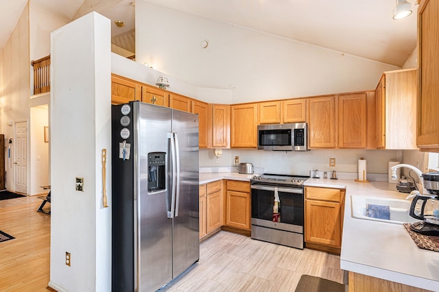 kitchen featuring sink, stainless steel appliances, light hardwood / wood-style flooring, and high vaulted ceiling