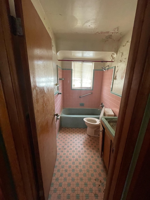 full bathroom featuring tile walls, toilet, tiled shower / bath, and vanity