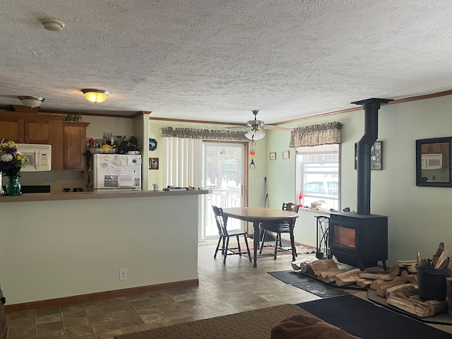 interior space featuring a wood stove, white appliances, ornamental molding, and brown cabinetry