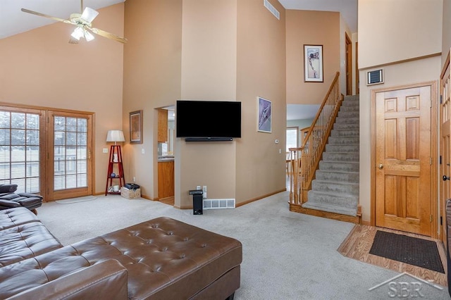 living room with ceiling fan, light carpet, and a towering ceiling