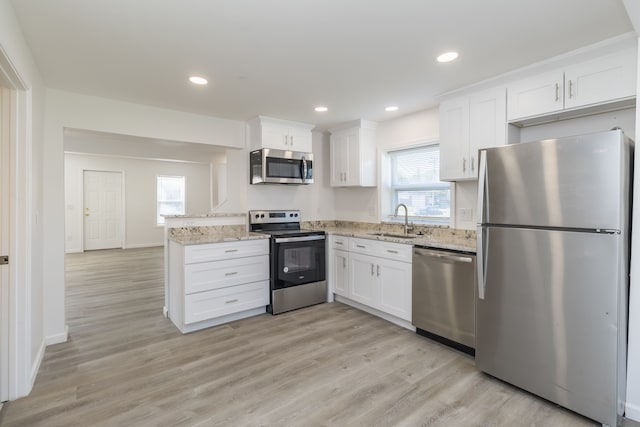 kitchen with sink, appliances with stainless steel finishes, white cabinetry, light stone countertops, and light wood-type flooring