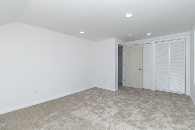 unfurnished bedroom featuring light carpet, lofted ceiling, and multiple closets