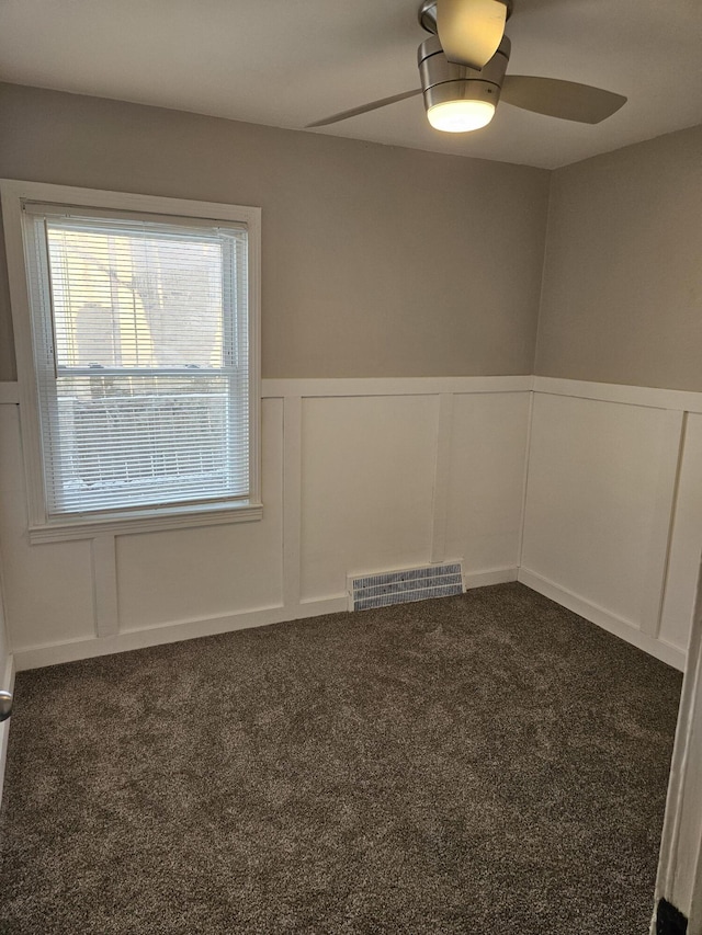 unfurnished room with ceiling fan and dark colored carpet