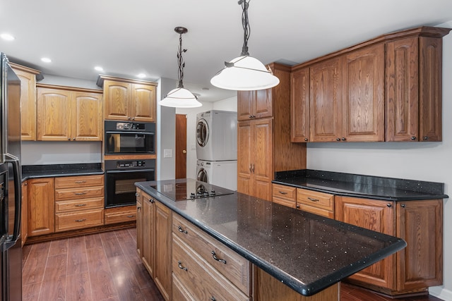 kitchen with dark wood-type flooring, decorative light fixtures, black appliances, a kitchen island with sink, and stacked washer and clothes dryer