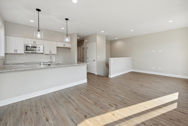 kitchen with light hardwood / wood-style floors, tasteful backsplash, decorative light fixtures, white cabinets, and light stone counters