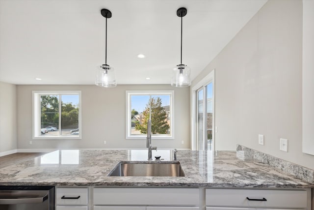 kitchen with pendant lighting, stainless steel dishwasher, white cabinetry, light stone countertops, and plenty of natural light