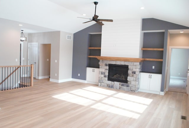 unfurnished living room with ceiling fan, built in shelves, vaulted ceiling, and a stone fireplace