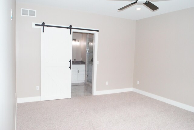 carpeted empty room with ceiling fan and a barn door