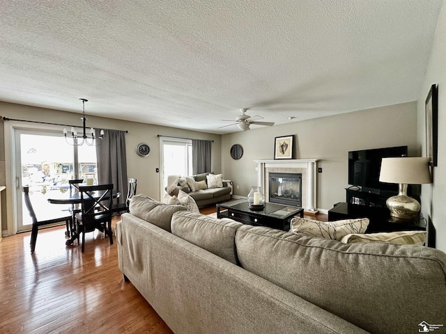 living room featuring ceiling fan with notable chandelier, a fireplace, light wood-type flooring, and a textured ceiling