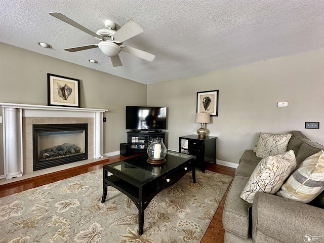 living room featuring a tiled fireplace, ceiling fan, a textured ceiling, and wood-type flooring