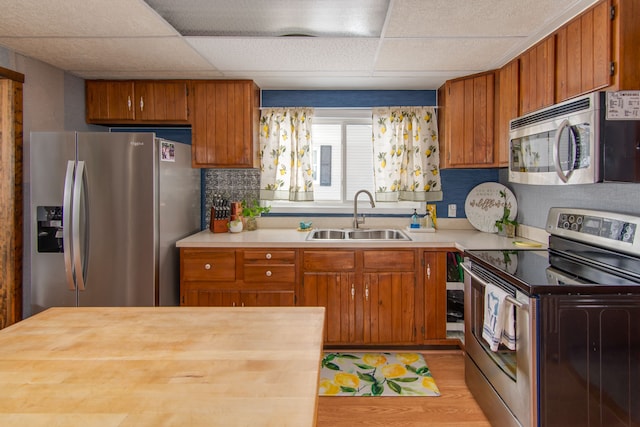 kitchen with stainless steel appliances, sink, a paneled ceiling, and light hardwood / wood-style flooring