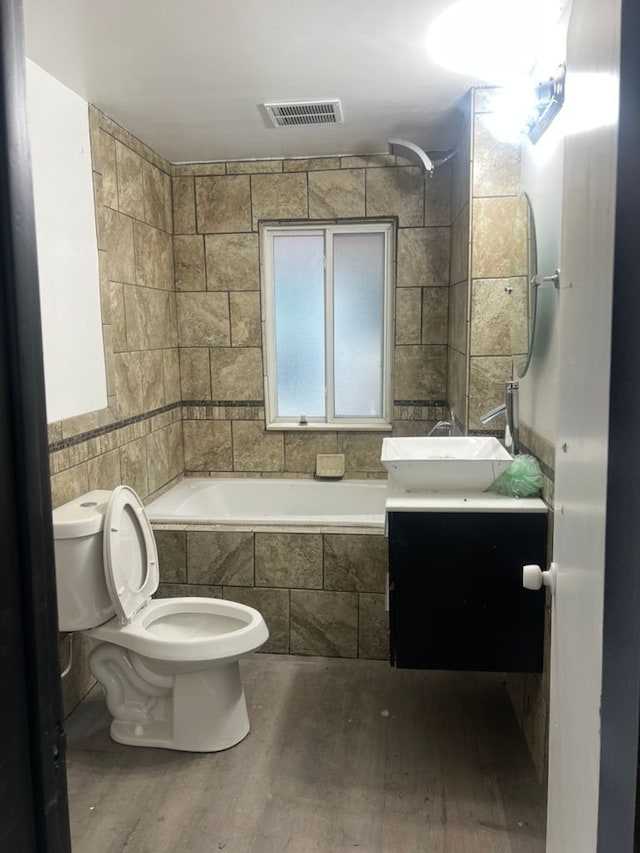 full bathroom featuring toilet, vanity, tile walls, and tiled shower / bath