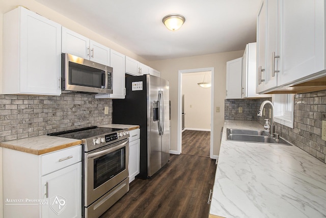 kitchen with appliances with stainless steel finishes, a sink, backsplash, white cabinets, and baseboards